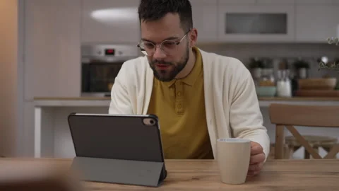 One man use digital tablet have video call online and hold cup at home Stock Footage 276477542