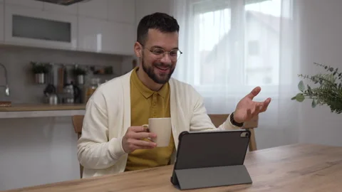 One man use digital tablet have video call online and hold cup at home Stock Footage 276477561