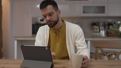 One man use digital tablet have video call online and hold cup at home Stock Footage 276477618