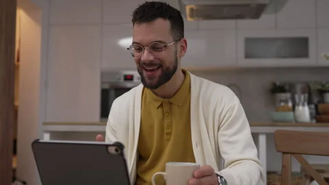 One man use digital tablet have video call online and hold cup at home Stock Footage 276477626