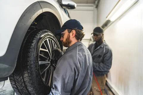 One mechanic replacing a tyre. Another mechanicn in the background. Blurred Foto stock