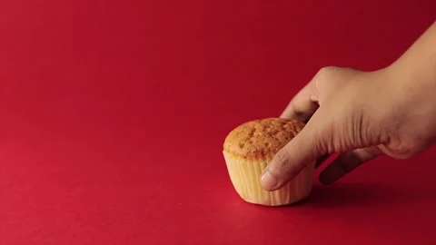 One muffin or cupcake picked up by hand and placing back. shot in red backgro Video stock 219973524
