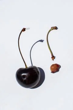 One normal red bing cherry next to one stem of an eaten cherry fruit. Stock Photos
