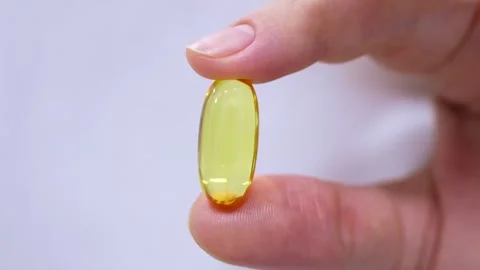 One omega-3 capsule (fish oil pill) in woman hand close up on white background Stock Footage 264095004