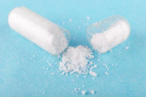 One open capsule of nutritional supplement msm, sulfur, on blue background Stock Photos