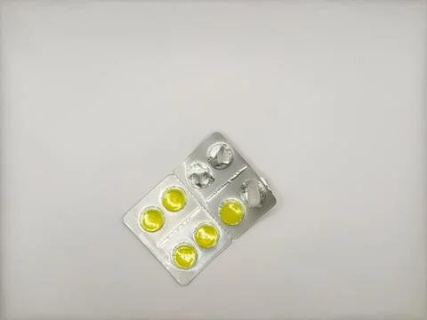 One open pack of bright yellow round tablets in silver packaging lies on white Stock Photos