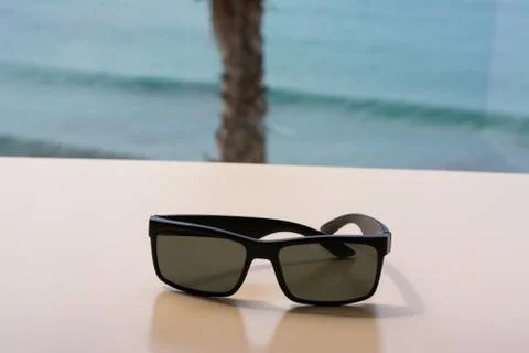 One pair of sunglasses on a table with a nice palm tree and the sea on the blurr Stock Photos