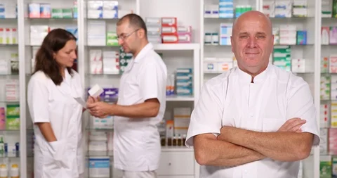 One Pharmacist Smiling to Camera and Two Pharmacists Talking in Background Stock Footage 109120745