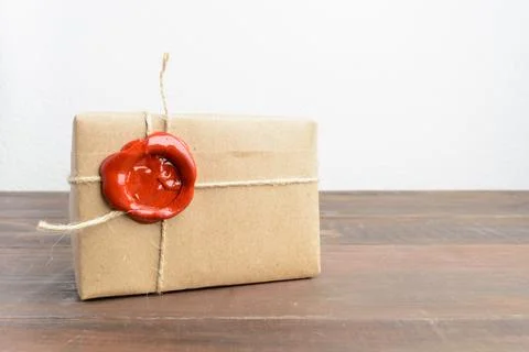 One present in craft paper with red sealing wax over wooden table Stock Photos