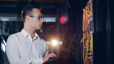 One programmer types on a laptop in a server room, close up. Stock Footage 99471299