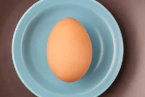 One raw egg on blue plate on brown background from top view with space for co Stock Photos