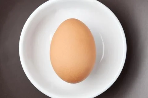 One raw egg on white plate on brown background from top view with space for c Stock Photos