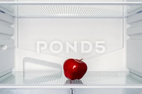 One red Apple on the shelf of an empty fridge. Weight loss and hunger concept Stock Photos