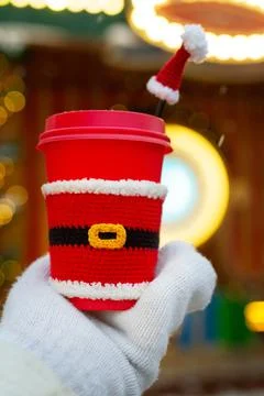 One red beige cups with white lid dressed in santa claus clothes in palm of hand Stock Photos