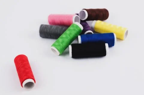 One red bobbin of thread near heap of bobbins of new colorful threads Stock Photos