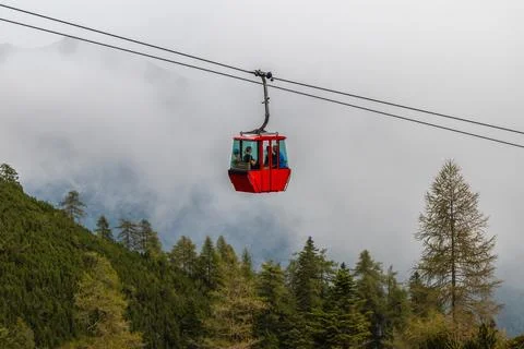 One red cable car cabin above the trees on a hill in the fog, Katrin cable car Stock Photos