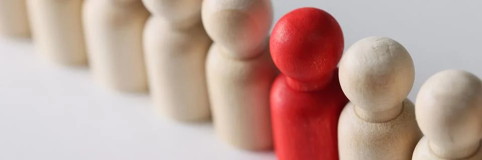 One red figure in row between wooden people figures 写真素材