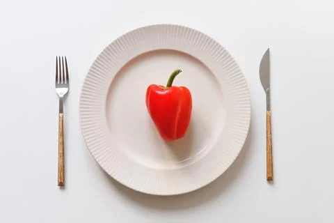 One red pepper in the dish. Fork and knife on white table. Vegan meal concept Stock Photos