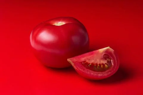 One red tomato, next to it lies a sliced slice of tomato. Stock Photos