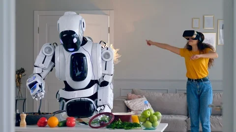 One robot cooks meal while a girl wears VR glasses. Stock Footage 113159542