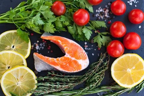 One salmon steak with greenery, lemon and cherry tomatoes on the black board Stock Photos