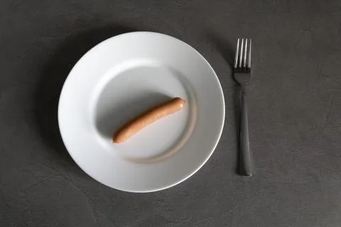 One sausage is impaled on a fork on a white plate with falling sunlight. Stock Photos