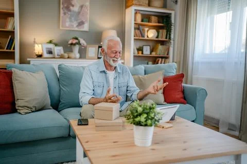 One senior man open box presents and read card while on video call Stock Photos