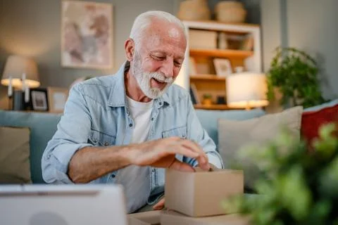 One senior man open box presents and read card while on video call Stock Photos