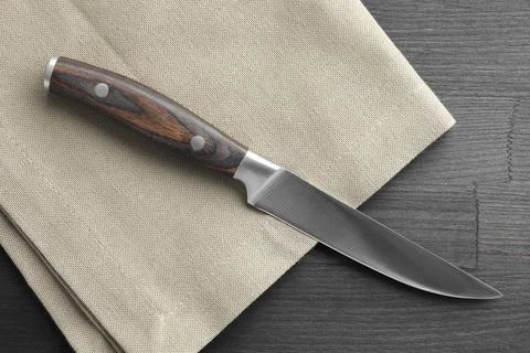 One sharp knife and napkin on black wooden table, top view Foto stock