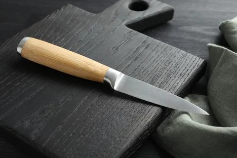 One sharp knife, cloth and board on black wooden table, closeup Foto stock