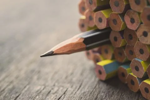 One sharpened pencil standing out from the other new pencil on wood table. Stock Photos