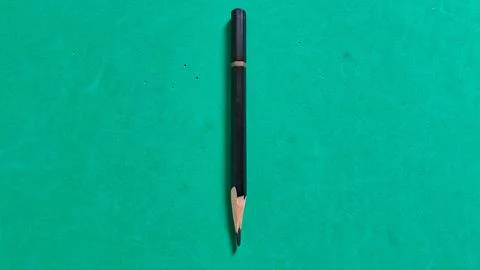 One single black sharpened wooden pencil on a green background Stock Photos