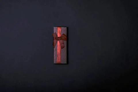 One single gift wrapped in dark brown paper with a bow of packthread on black Stock Photos