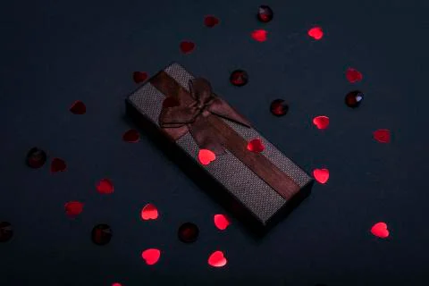 One single gift wrapped in dark brown paper with a bow of packthread on black Stock Photos