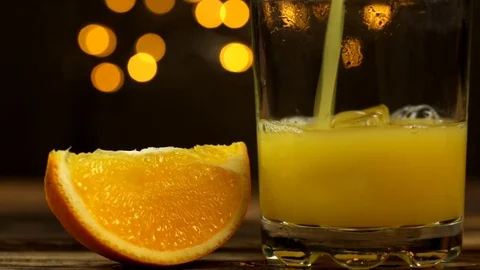 One slice of orange and juice is poured into a glass with lights in the back Video stock 123590523