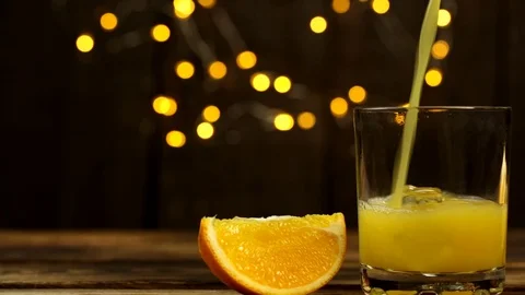 One slice of orange and juice is poured into a glass with lights in the back Video stock 123590615