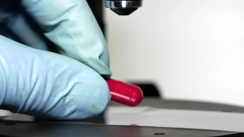 One of three microscope objectives is lowered onto a red pill in macro Stock Footage 317310636