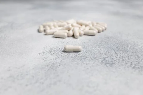 One white capsule of cure on background of bunch of pills unfocused Stock Photos