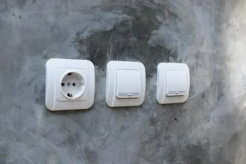 One white electrical power socket and two light switches mounted on a raw p.. Stock Photos