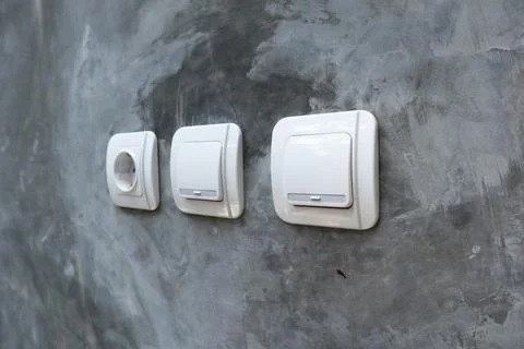 One white electrical power socket and two light switches mounted on a raw p.. Stock Photos