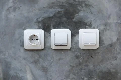One white electrical power socket and two light switches mounted on a raw p.. Stock Photos