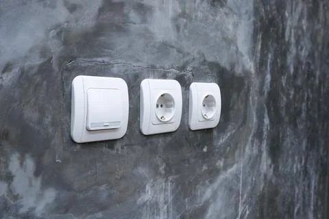 One white light switch and two electrical outlets mounted on a raw polished.. Stock Photos
