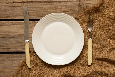 One white plate and a fork with a knife lie on an old wooden table in the kit Stock-Fotos