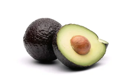 One whole and one half cut avocados are rotating on the turntable. Isolated on Stock Footage 157039338