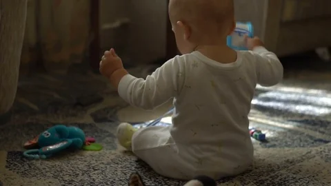 A one year age baby boy sitting on floor in sunny living room and playing Stock Footage