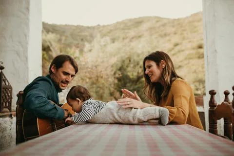 One year infant lying down on a courtyard table while his father plays guitar Stock Photos
