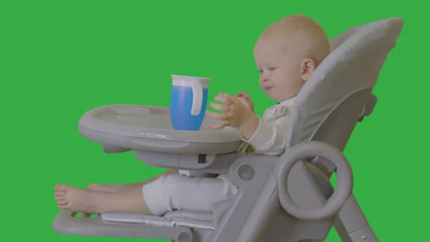 One year old baby boy drinking water sitting on high chair on green screen 1 Stock Footage 265954530