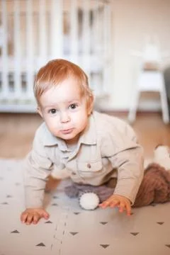 A one-year-old boy in a beige shirt and sitting on the floor Stock Photos