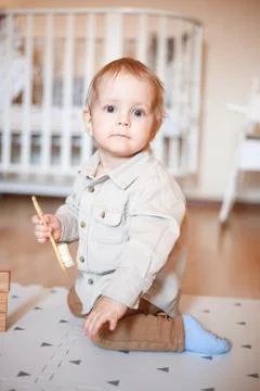 A one-year-old boy in a beige shirt and sitting on the floor Stock Photos