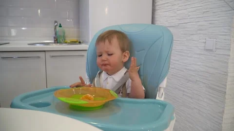 A one-year-old boy eats mandarin slices with his hands from a plate while sittin Stock Footage 302832817